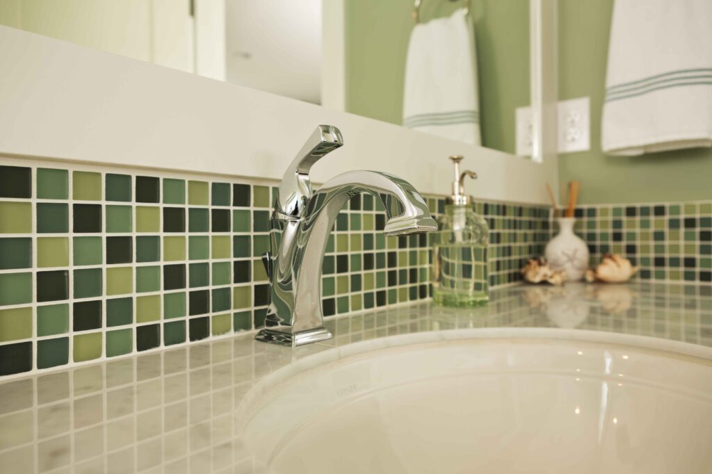 Green mosaic tiles surrounding white sink with chrome tap