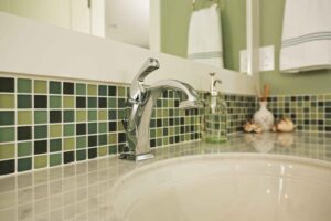 Green mosaic tiles surrounding white sink with chrome tap