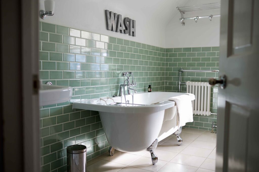 Bathroom with green metro tiles, roll top bath, chrome features.