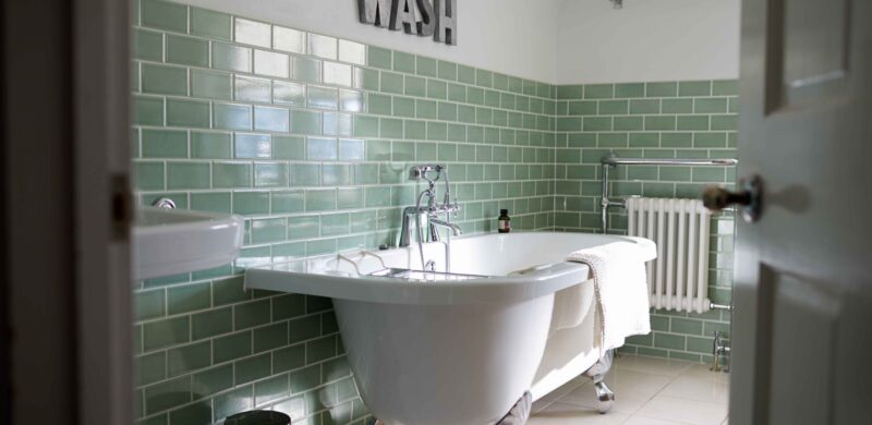 Bathroom with green metro tiles, roll top bath, chrome features.