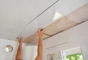 Worker installing PVC ceiling panels in a bathroom.