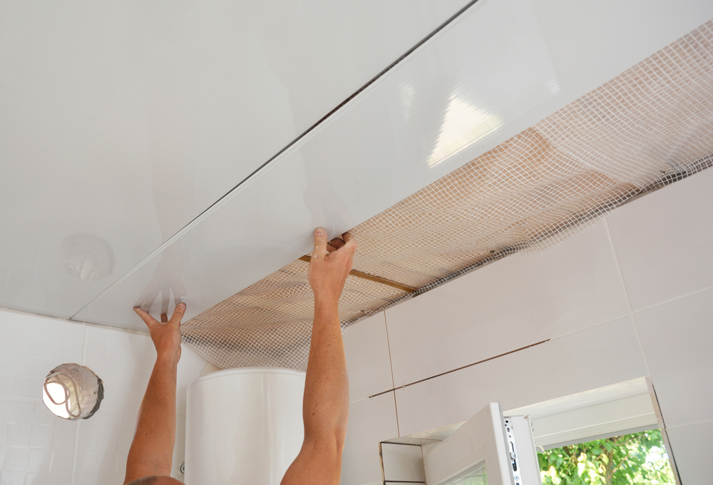 Worker installing PVC ceiling panels in a bathroom.